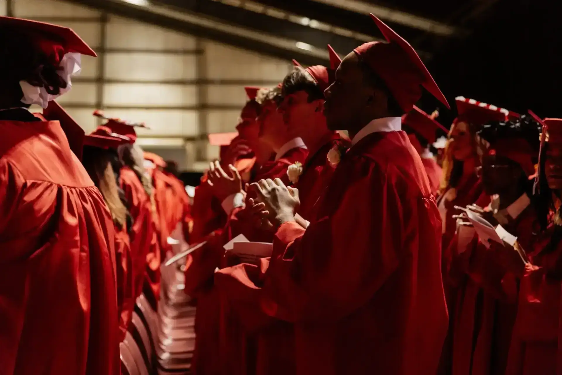 Graduates in red caps and gowns stand in rows, facing forward.